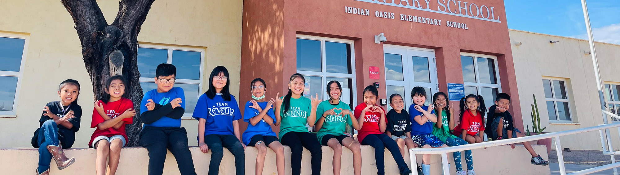 Happy students sitting on wall outside front of school wearing team t-shirts